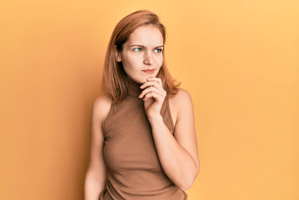 Young caucasian woman wearing casual style with sleeveless dress thinking concentrated about doubt with finger on chin and looking up wondering  - Foto, Bild