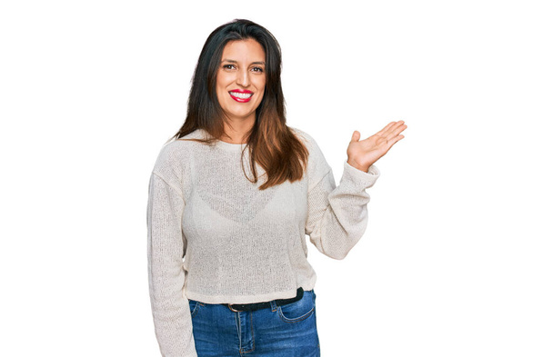 Piękna Latynoska kobieta ubrana w luźny sweter uśmiechnięta, radosna prezentacja i wskazująca dłonią na aparat fotograficzny.  - Zdjęcie, obraz