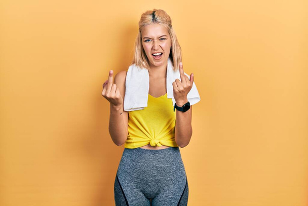 Beautiful blonde sports woman wearing workout outfit showing middle finger doing fuck you bad expression, provocation and rude attitude. screaming excited  - Foto, imagen
