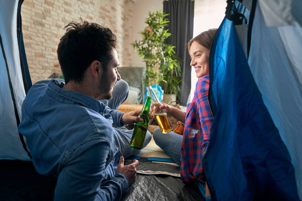 自宅でテントの中でビールと座っているカップルの後部ビュー                                - 写真・画像