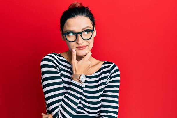 Young caucasian woman wearing casual clothes and glasses with hand on chin thinking about question, pensive expression. smiling with thoughtful face. doubt concept.  - Photo, Image