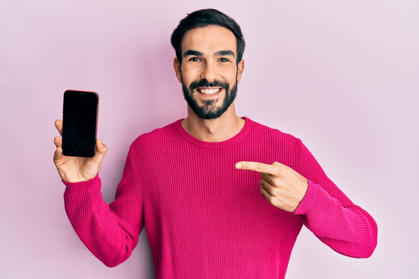 Giovane uomo ispanico in possesso di smartphone mostrando schermo bianco sorridente con un sorriso felice e fresco sul viso. mostrando i denti.  - Foto, immagini