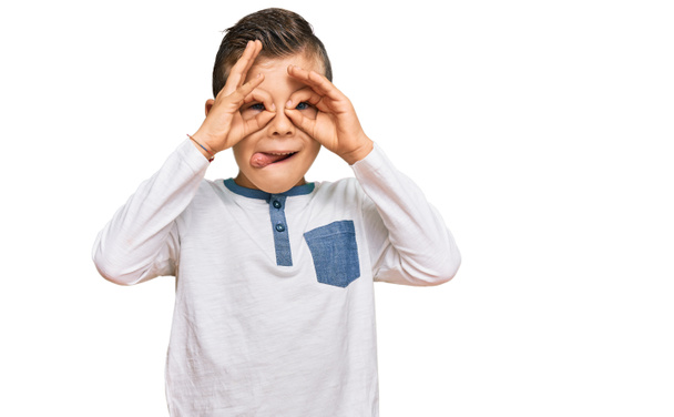 Чарівний кавказький дитина в повсякденному одязі робить нормальний жест, як бінокль, що стирчить язиком, очі дивляться крізь пальці. божевільний вираз
.  - Фото, зображення