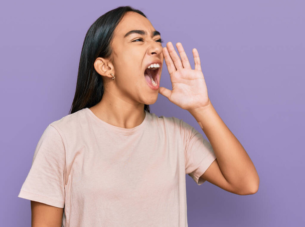Junge asiatische Frau in lässiger Kleidung schreit und schreit laut mit der Hand auf dem Mund zur Seite. Kommunikationskonzept.  - Foto, Bild