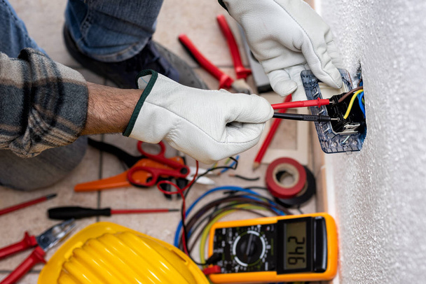 View from above. Electrician worker at work with the tester measures the voltage in an electrical system. Working safely with protective gloves. Construction industry. - Photo, Image