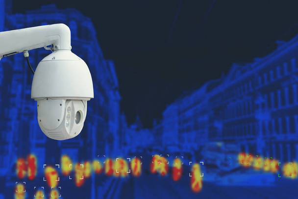 The concept of video surveillance and security technology. CCTV camera on the background of the city road with cars and definition people. Night tint. - Photo, Image