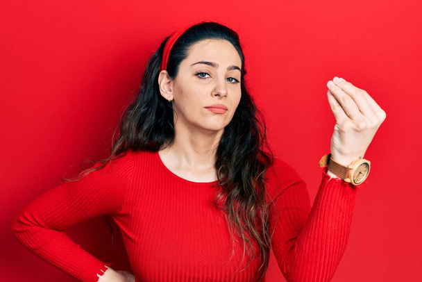 Молодая латиноамериканка, одетая в повседневную одежду, делает итальянский жест с уверенным выражением рук и пальцев  - Фото, изображение