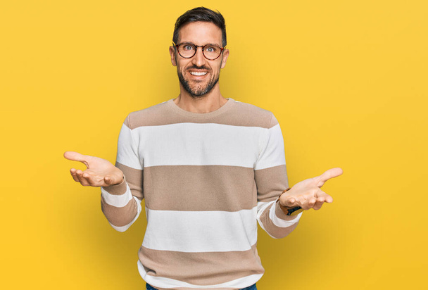 Handsome man with beard wearing casual clothes and glasses smiling cheerful with open arms as friendly welcome, positive and confident greetings  - Photo, Image