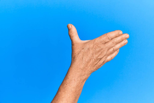 Mano del hombre hispano mayor sobre fondo azul aislado presentando con la palma abierta, buscando apoyo y ayuda, gesto de asistencia  - Foto, imagen