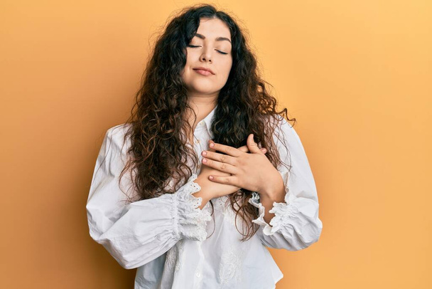 Young brunette woman with curly hair wearing casual clothes smiling with hands on chest, eyes closed with grateful gesture on face. health concept.  - Photo, Image
