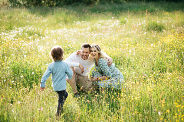 緑の草原の外で一緒に花と幸せな若い家族の時間を過ごす屋外。家族の休日の概念. - 写真・画像