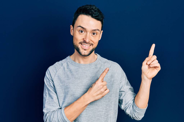 Young hispanic man wearing casual clothes smiling and looking at the camera pointing with two hands and fingers to the side.  - Photo, image