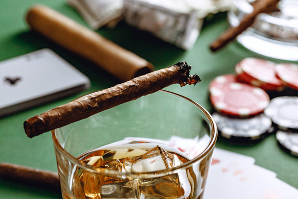 Cuban cigar, whiskey glass and chips on table - Fotó, kép