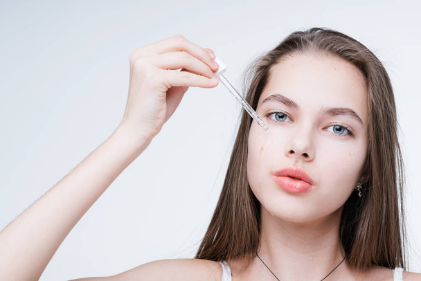 Beautiful young girl holding a dropper with serum in her hands, applying it to her face - Foto, Imagem
