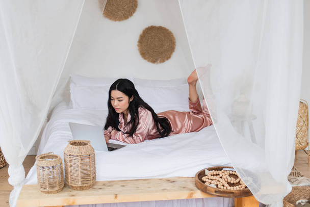 joven asiático mujer acostado en blanco cama con portátil en dormitorio - Foto, Imagen