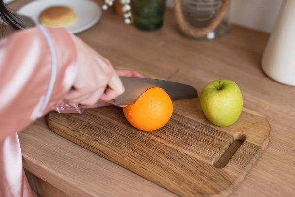 close up view of young female hands cutting fruits in kitchen - Foto, afbeelding