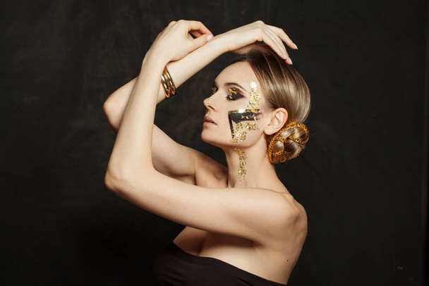 Attraente donna modello bruna con trucco creativo e acconciatura updo con catena d'oro su sfondo nero - Foto, immagini