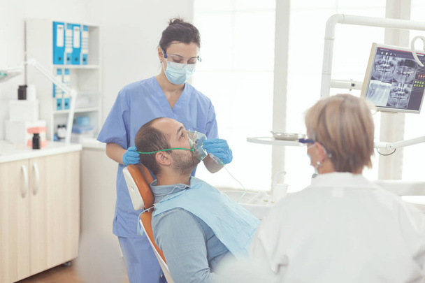 Stomatologist nurse putting oxigen mask to patient examining toothache - Photo, Image