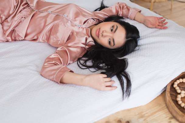 ベッドルームで手を伸ばして白いリネンの上に横たわる若いアジア人女性の高い角度のビュー - 写真・画像
