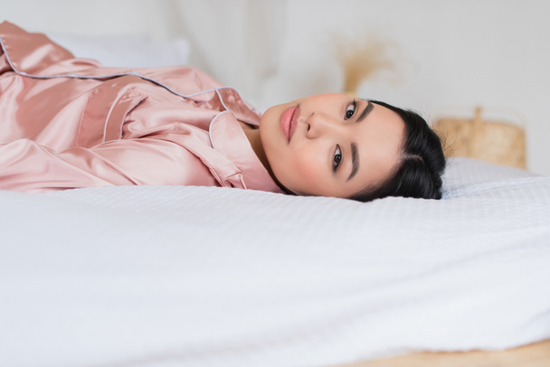 nuori aasialainen nainen makaa sängyllä ja katselee kameraa makuuhuoneessa - Valokuva, kuva