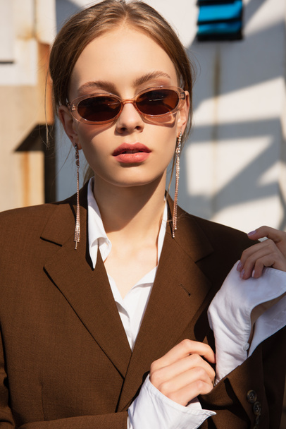 pretty young model with earrings in sunglasses posing on rooftop  - Φωτογραφία, εικόνα