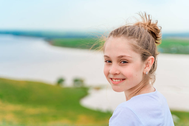 Rückansicht eines kleinen Mädchens auf einer grünen Wiese mit herrlichem Blick auf die Hügel und den Fluss - Foto, Bild