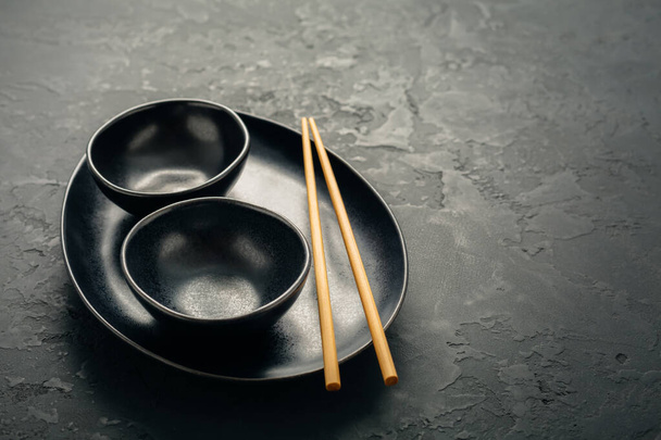 Pottery bowls or ceramics in blacke tone with chopsticks on black background. Kitchenware - Фото, изображение