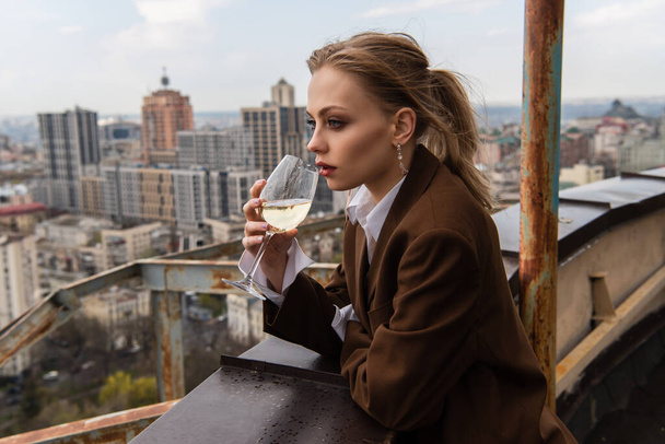 young woman drinking wine on rooftop with cityscape on blurred background - Fotó, kép