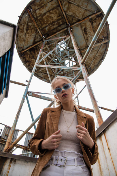 low angle view of trendy model in blue sunglasses posing near construction on rooftop - 写真・画像