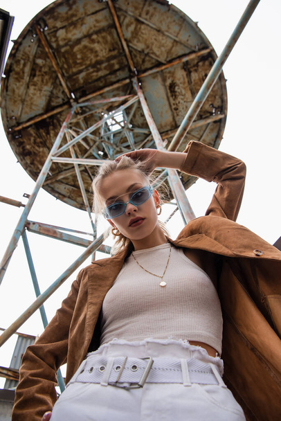 low angle view of young model in blue sunglasses posing near construction on rooftop - 写真・画像