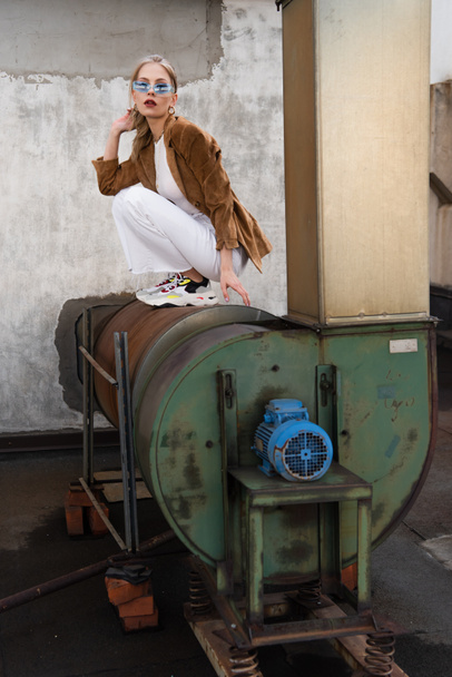 full length of young model in stylish outfit and blue sunglasses posing on rusty construction  - Foto, Imagem