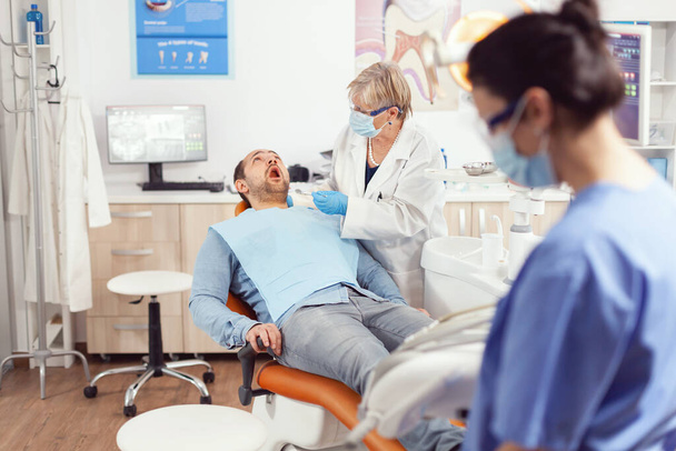 Stomatolog starszy lekarz patrzący w ustach pacjenta przygotowujący się do badania stomatologicznego. - Zdjęcie, obraz