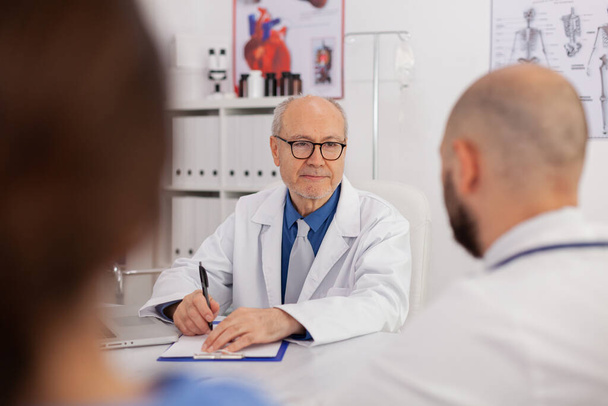 Портрет лікаря старшого чоловіка, який обговорює з командою лікарні роботу над медичною експертизою
 - Фото, зображення