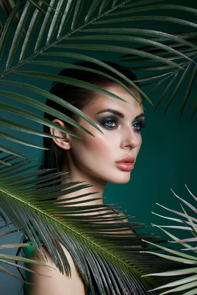 Tropical portrait sexy woman in leaves palm tree. Bright green makeup, shadow of palm leaves on girl face. Beautiful makeup - Foto, Imagem