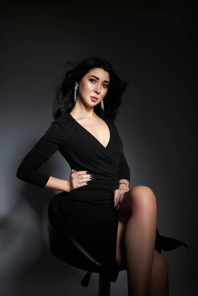 Beautiful brunette woman in a black dress poses in the studio. Elegant girl with beautiful natural makeup - Foto, immagini