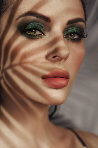 Shadow of palm leaves on girl face. Beautiful makeup. Tropical portrait sexy woman in leaves palm tree. Bright green makeup - Φωτογραφία, εικόνα