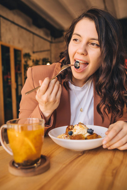 sourire belle femme dans le café manger gâteau avec crème glacée et myrtilles thé orange dans une tasse - Photo, image