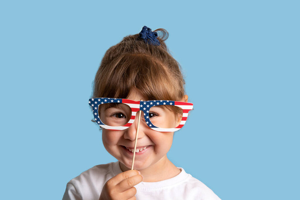 Baby girl smiling with USA flag glasses on blue background - Фото, изображение
