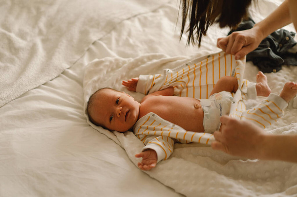新生児の赤ちゃんを変えるお母さん。ベッドの上でおむつを変えながら赤ちゃんと遊ぶ幸せな若い母親。幸せな母親。幼児の赤ちゃん。母の日 - 写真・画像