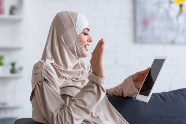 muslim woman waving hand during video call on digital tablet at home - Foto, imagen
