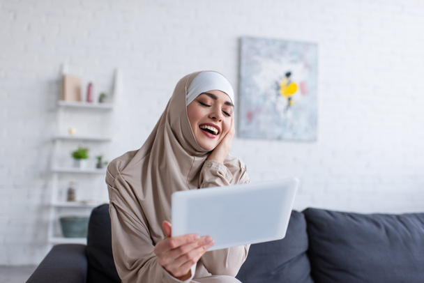 excited muslim woman laughing near digital tablet at home - Φωτογραφία, εικόνα