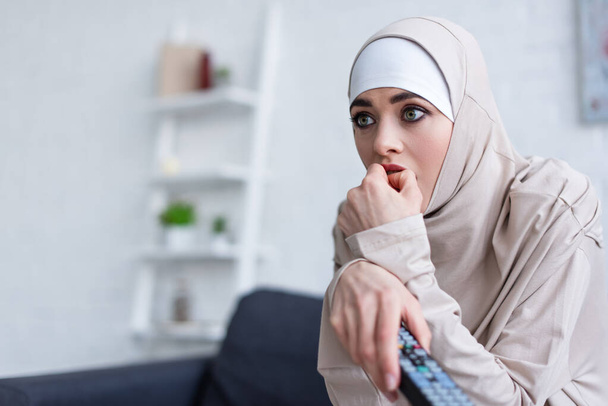 nervous arabian woman holding hand near face while watching tv at home - Zdjęcie, obraz