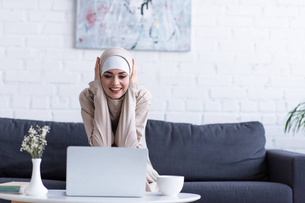 Мусульманская женщина улыбается, глядя на ноутбук дома - Фото, изображение