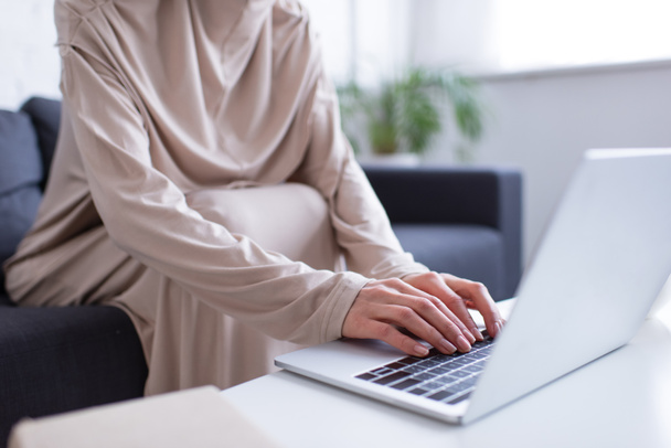 καλλιεργημένη άποψη του muslim γυναίκα δακτυλογράφηση σε φορητό υπολογιστή σε θολή πρώτο πλάνο - Φωτογραφία, εικόνα