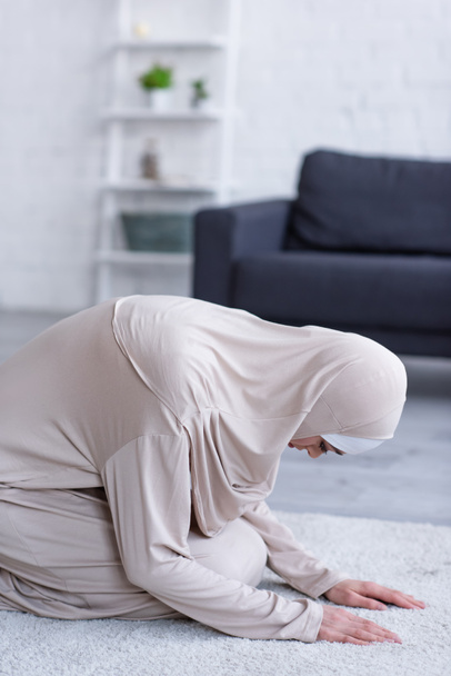 Μουσουλμάνα γυναίκα με χιτζάμπ και αμπάγια προσεύχεται στο χαλί στο σπίτι - Φωτογραφία, εικόνα