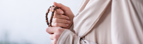 vista ritagliata della donna musulmana con rosario che prega a casa, striscione - Foto, immagini