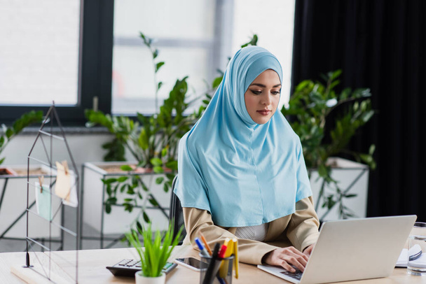 young muslim woman typing on laptop in office on blurred foreground - 写真・画像