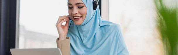 mulher muçulmana alegre ajustando fone de ouvido enquanto trabalhava no call center, banner - Foto, Imagem