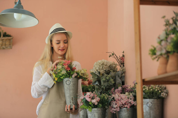 Блондинка с волосами уверенно стоит перед цветком в открытом цветочном магазине. Концепция малого бизнеса. - Фото, изображение