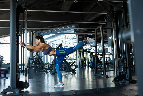 Sporty girl effectuer debout extension de la hanche dans le câble crossover à la salle de gym - Photo, image